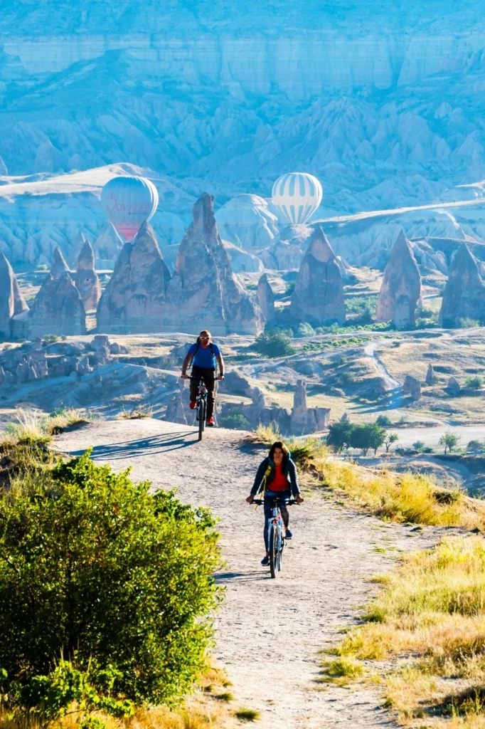 Cyclists riding through Cappadocia with hot air balloons in the background.