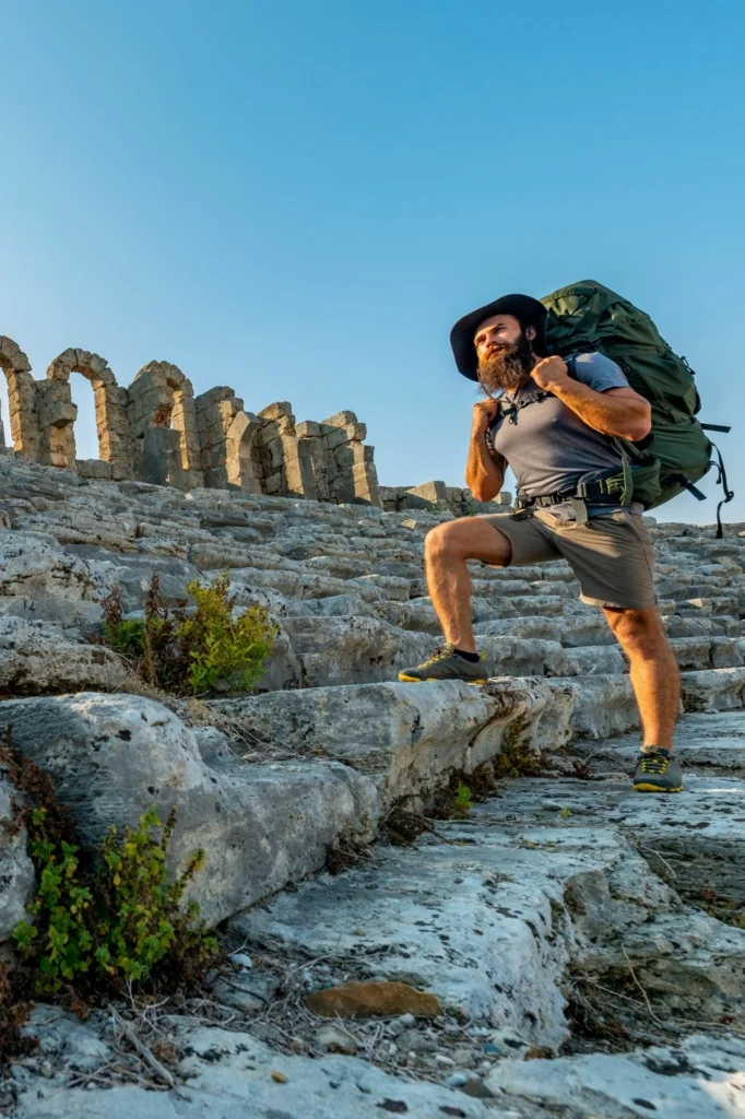 Hiker with backpack exploring ancient ruins under a clear sky.
