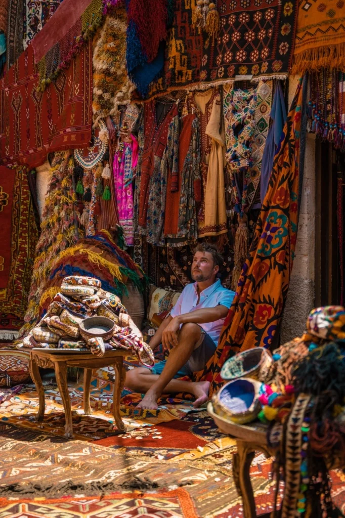 Man sitting among colorful Turkish carpets and textiles.