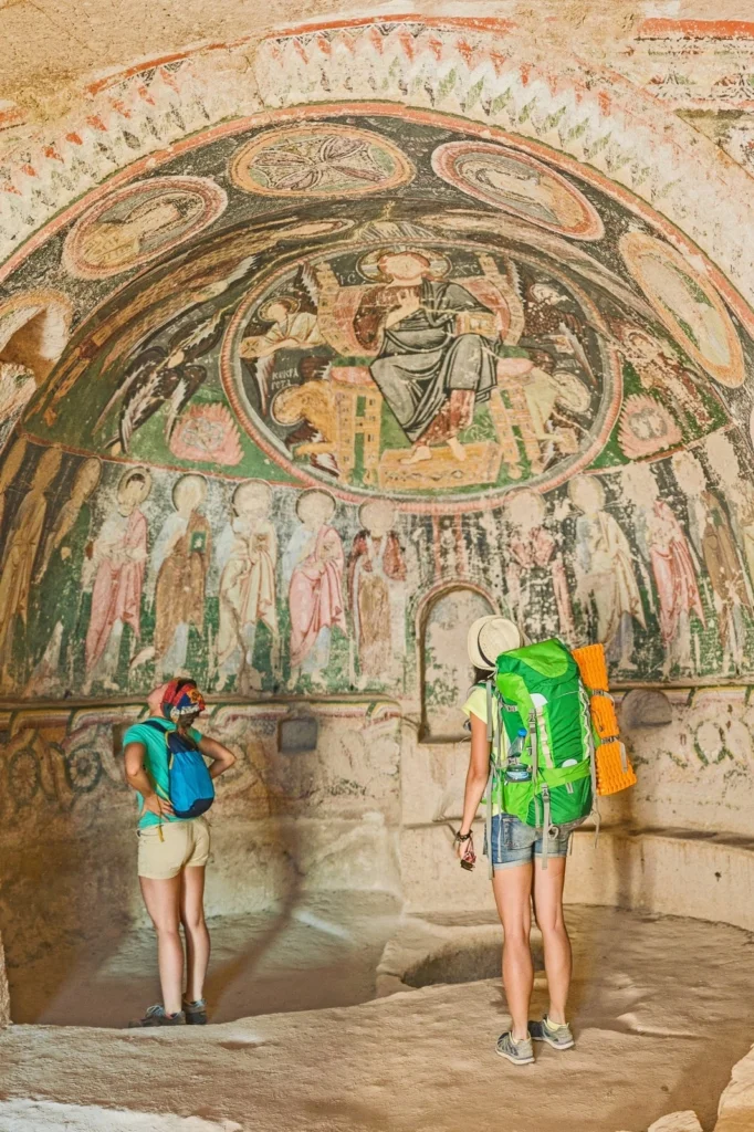 Tourists viewing ancient frescoes in Cappadocia cave.