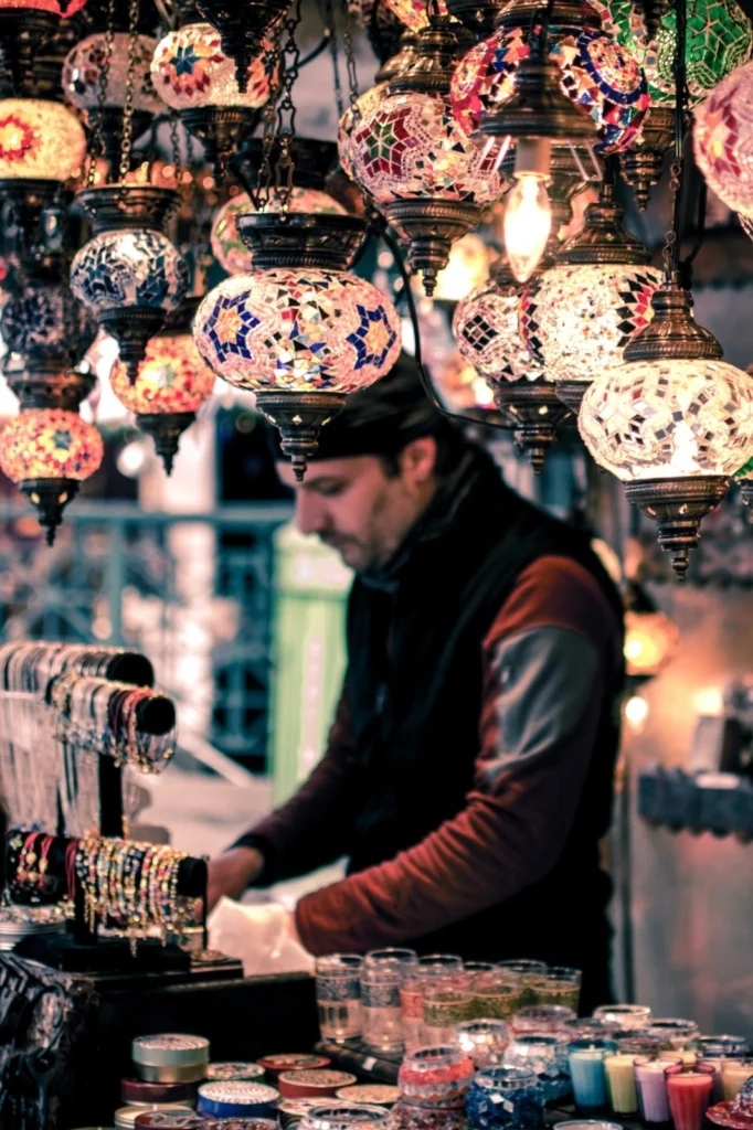 Vendor selling colorful mosaic lamps and bracelets at a market stall.