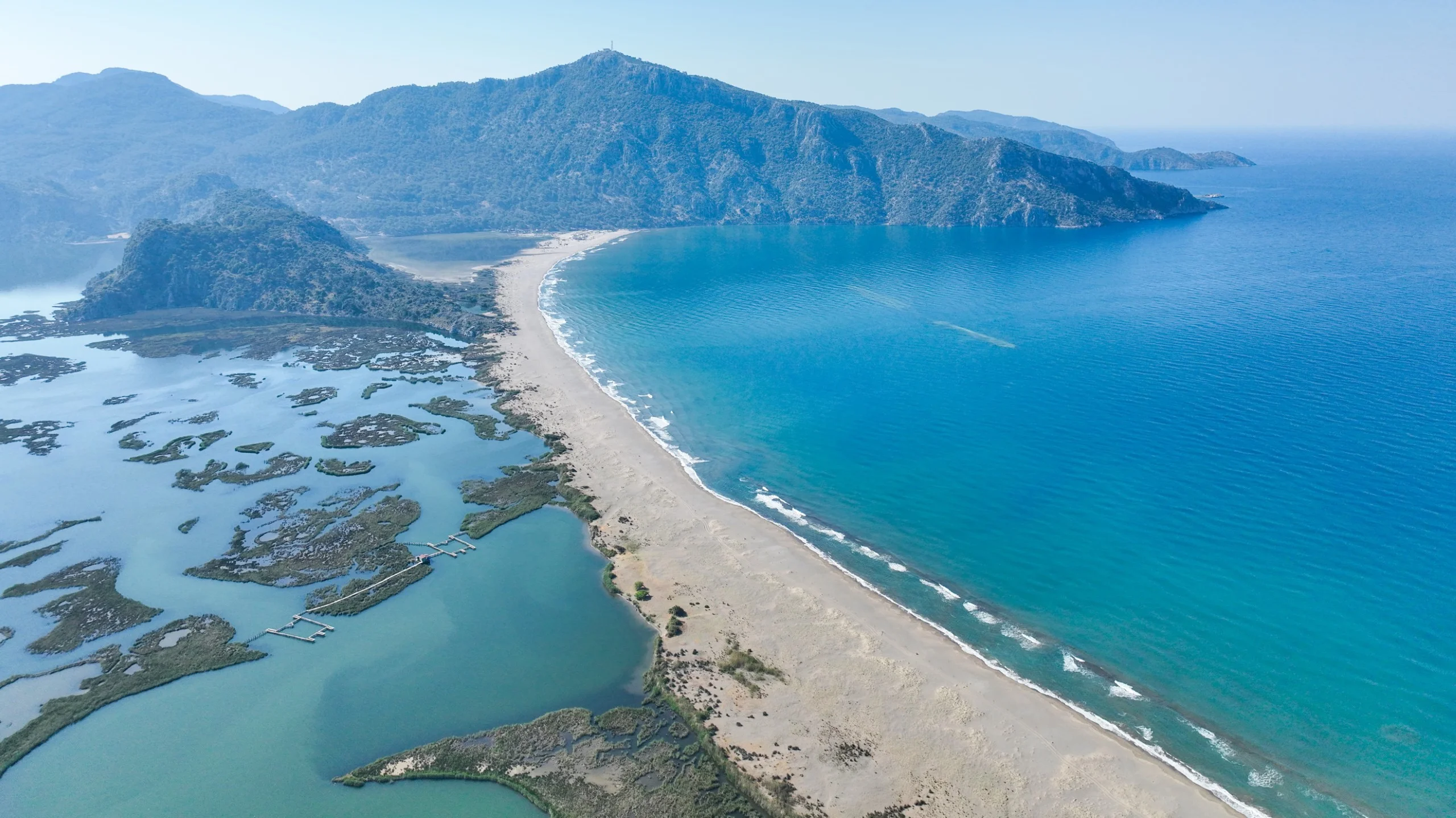 Aerial view of Iztuzu Beach with surrounding mountains and clear blue sea.