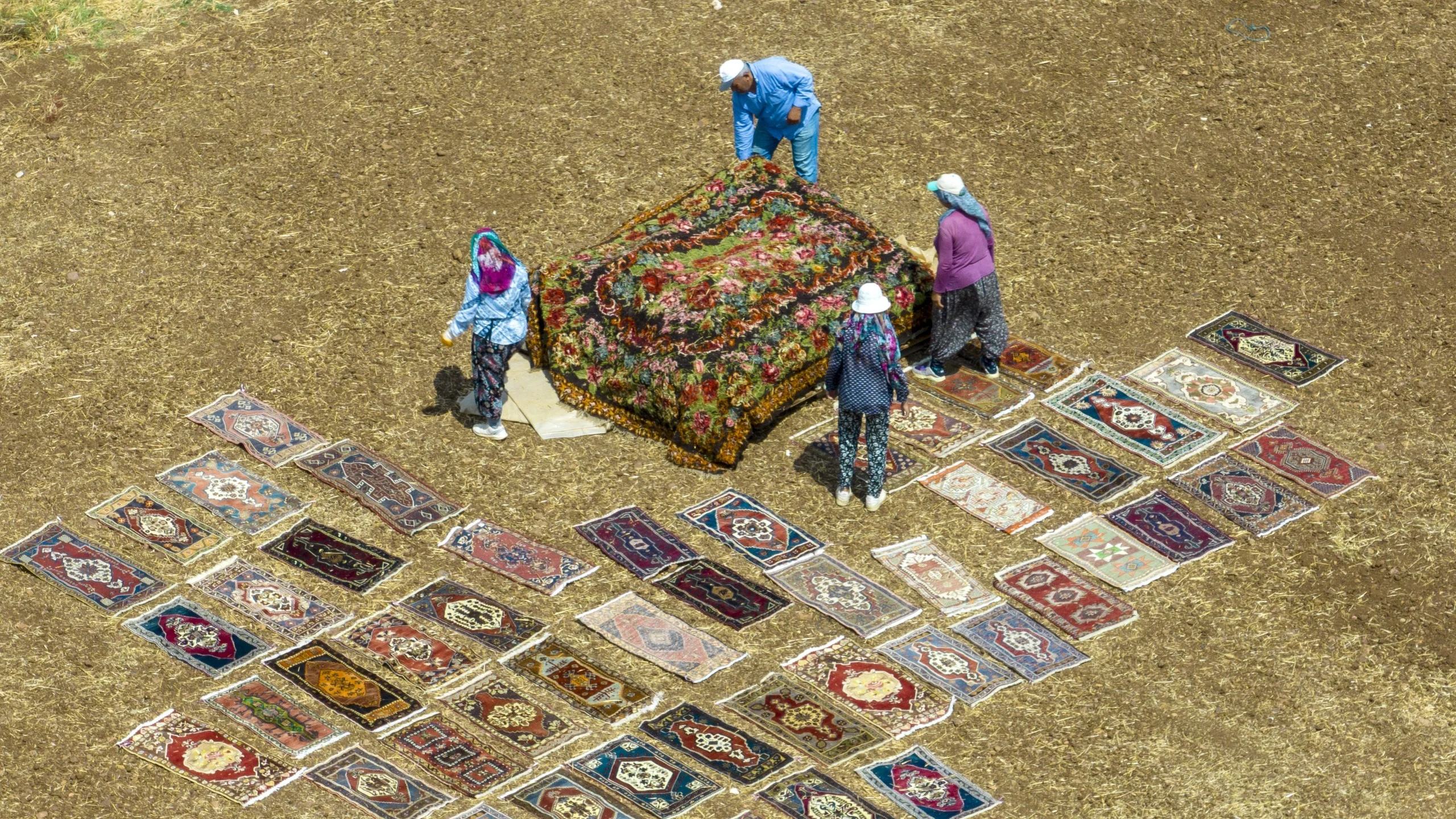 Aerial view of people arranging colorful rugs on the ground.