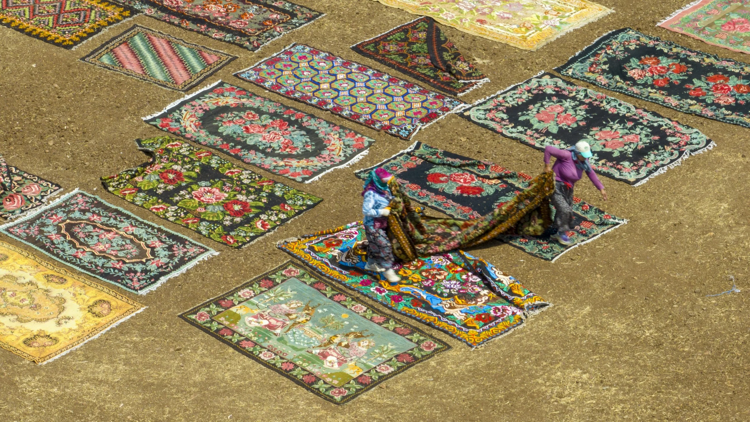 Colorful Turkish carpets drying under the sun with two people arranging them.