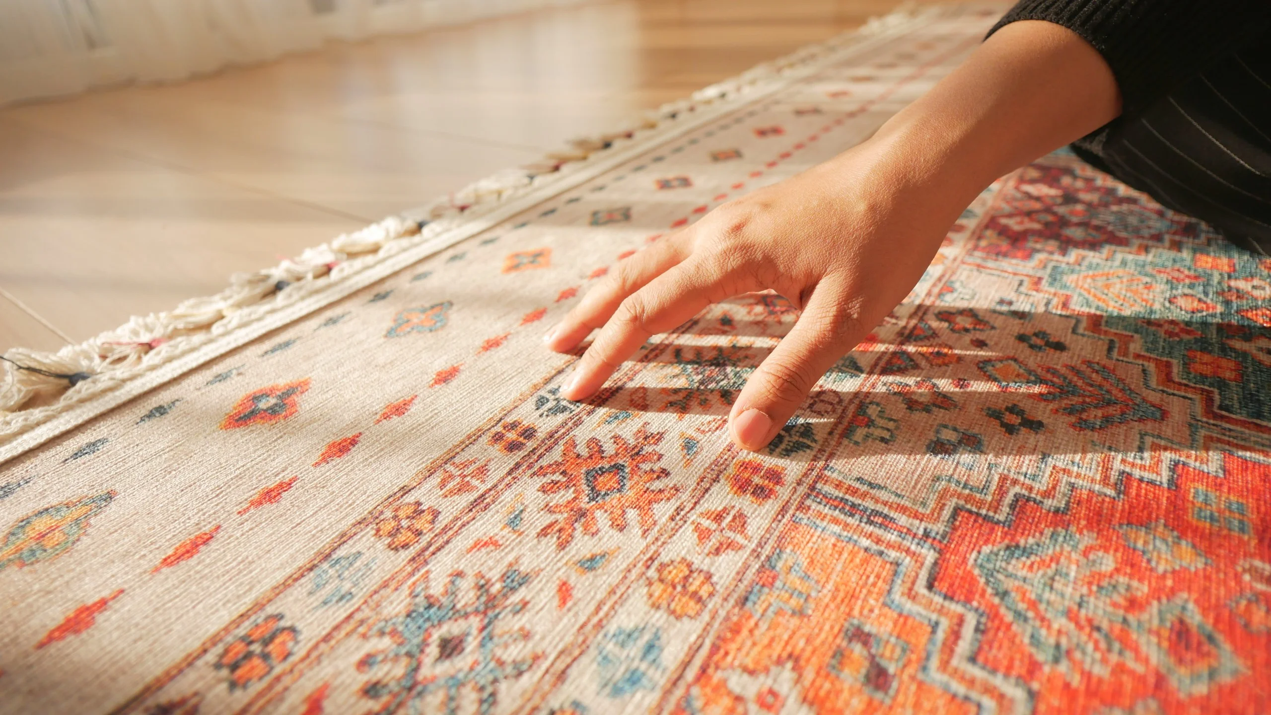 Hand touching a colorful patterned carpet with intricate designs.
