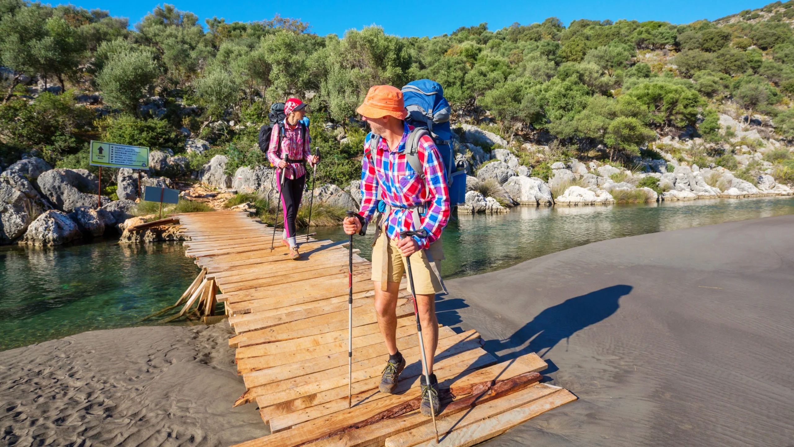 Hikers crossing a wooden bridge over a scenic river.