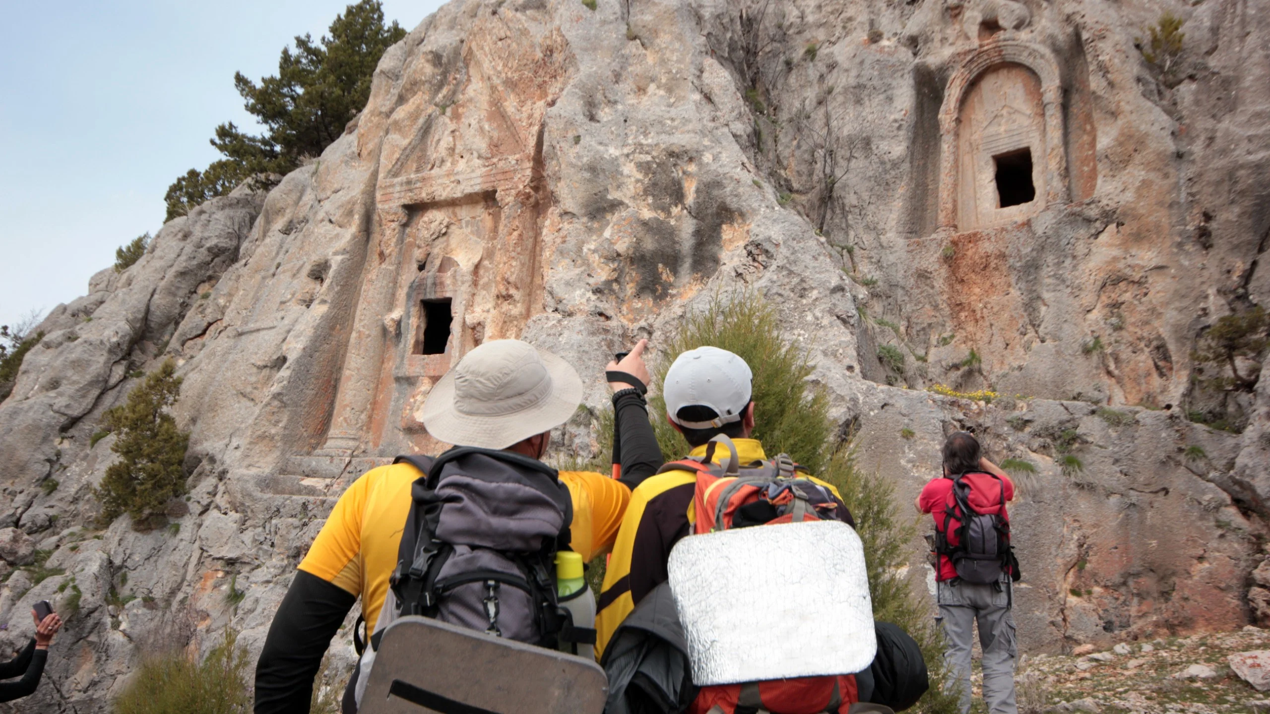 Hikers exploring ancient rock carvings on a cliff.