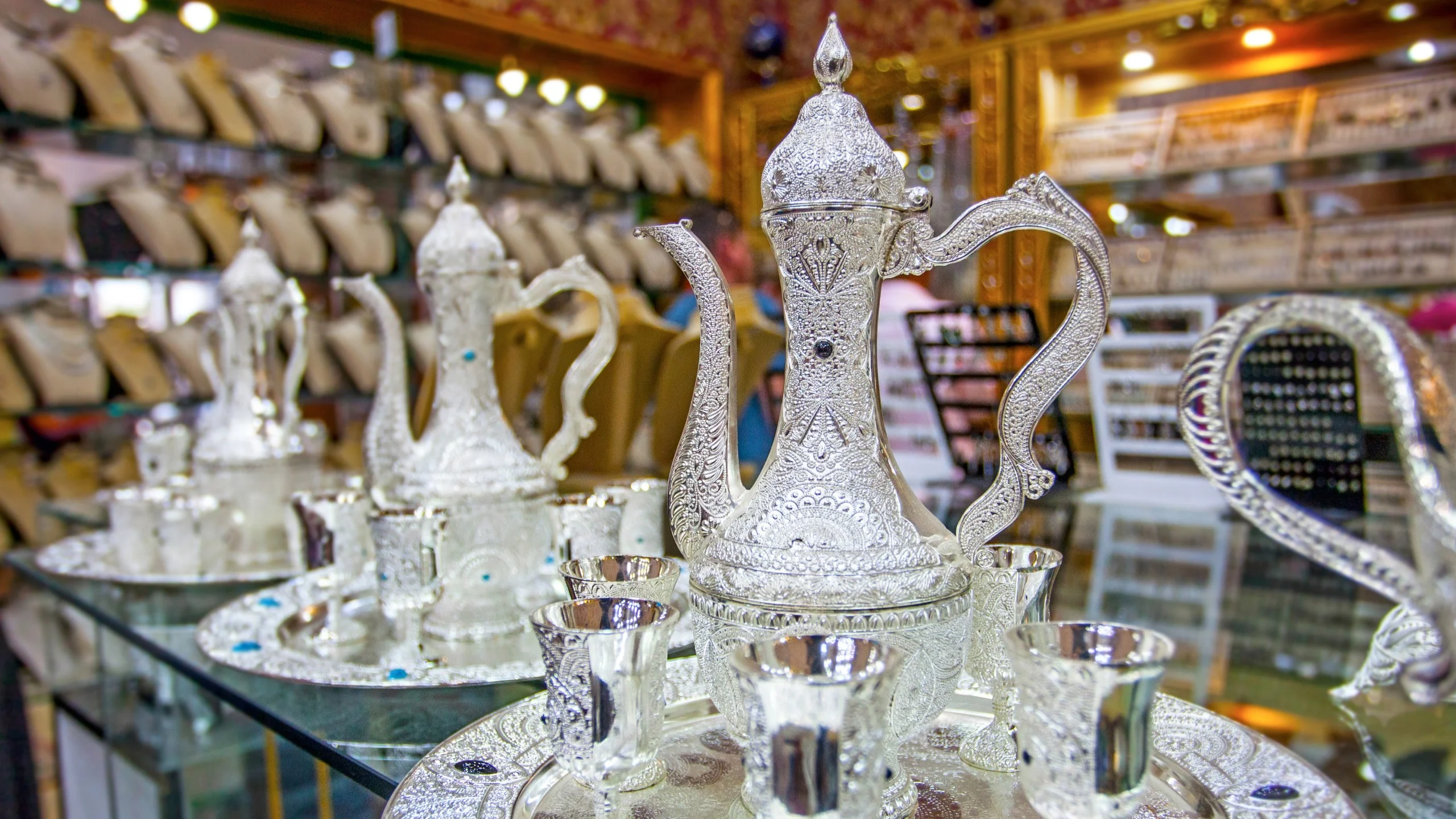 Intricately designed silver pot with cups in a shop display.