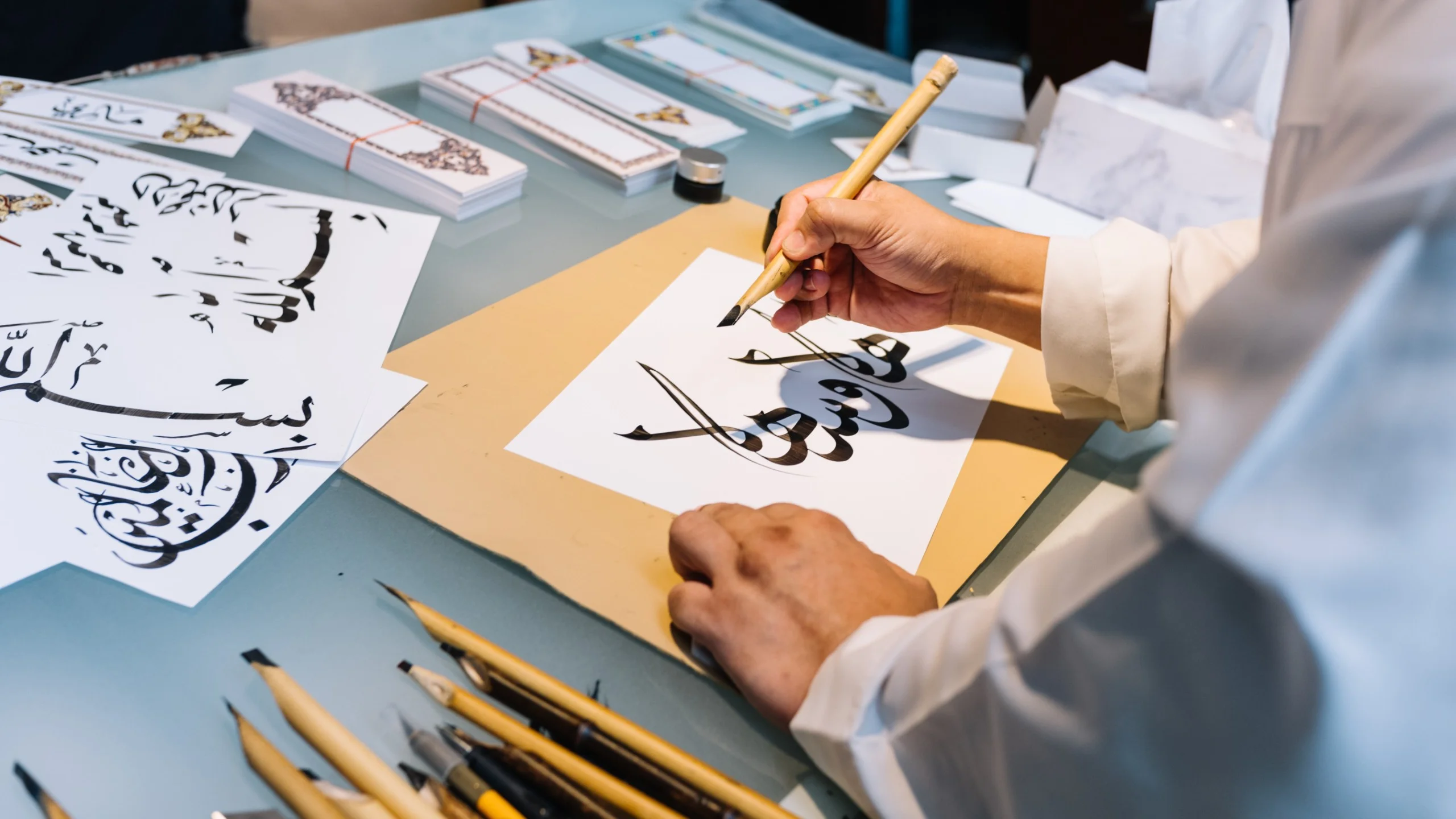 Person practicing traditional Arabic calligraphy with bamboo pens.