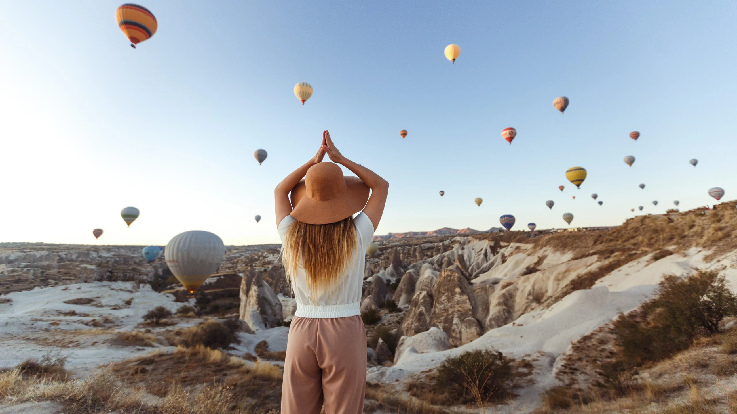 Woman in hat enjoying hot air balloons over Cappadocia landscape