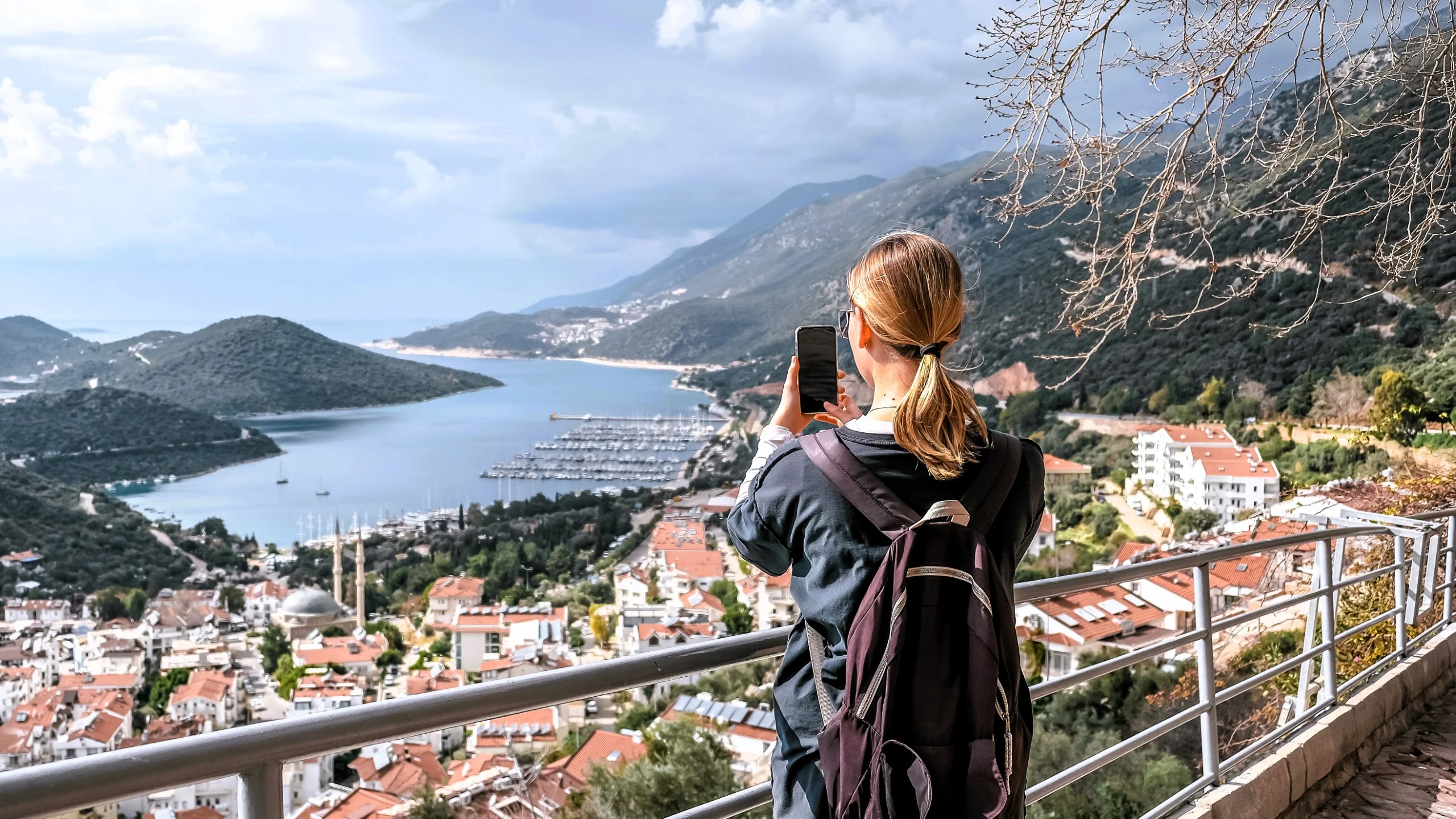 Woman hiking solo, photographing a scenic coastal town.