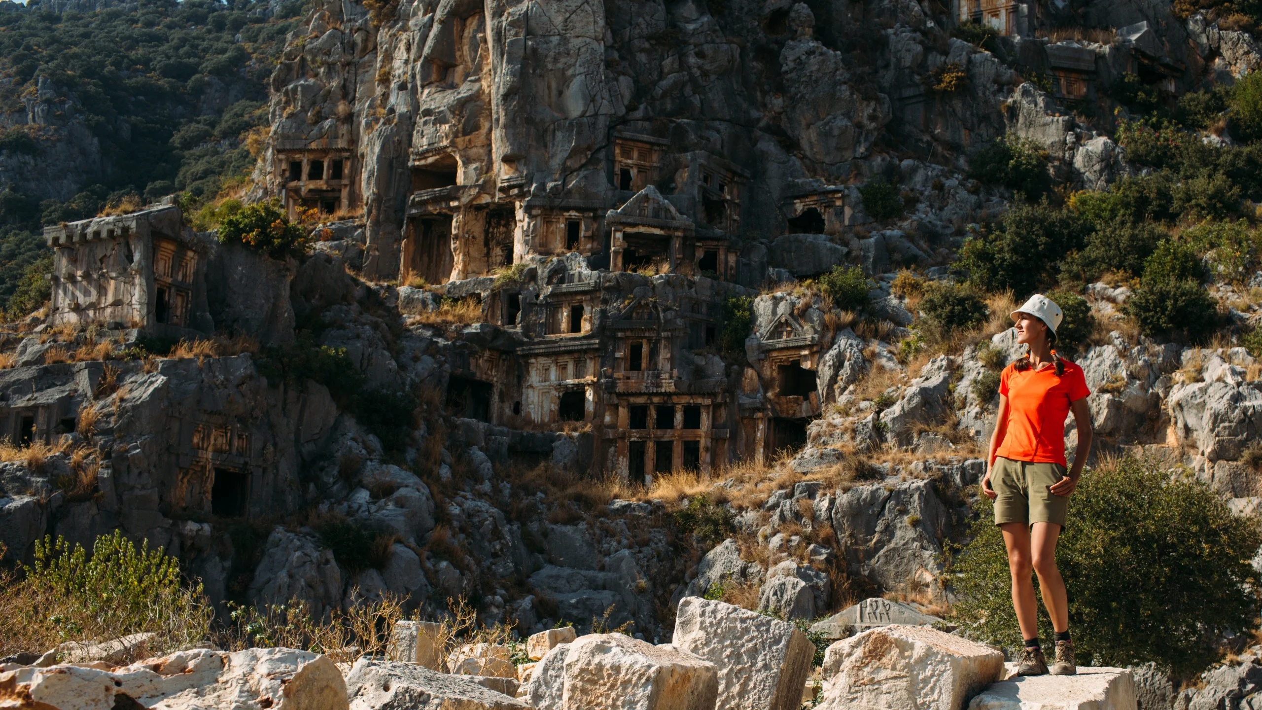 Woman traveler exploring ancient rock-cut tombs in a mountainous region.